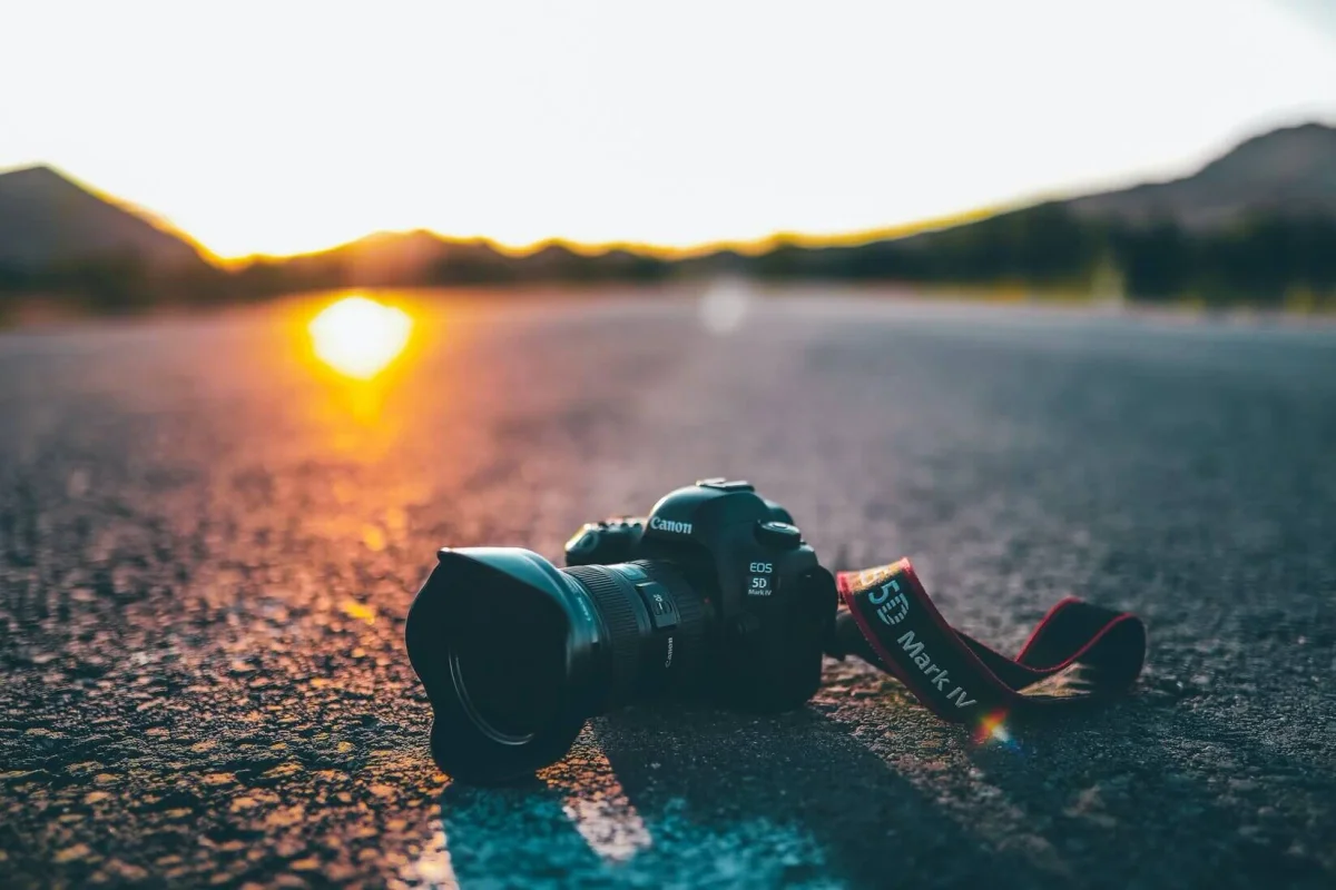 Canon camera lying on a road with the sun setting in the background, casting a warm glow.