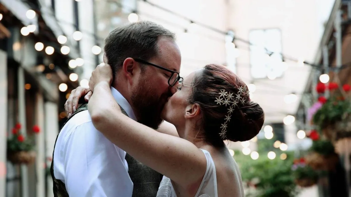 Bride and groom kissing in a courtyard lit with string lights and hanging flower baskets