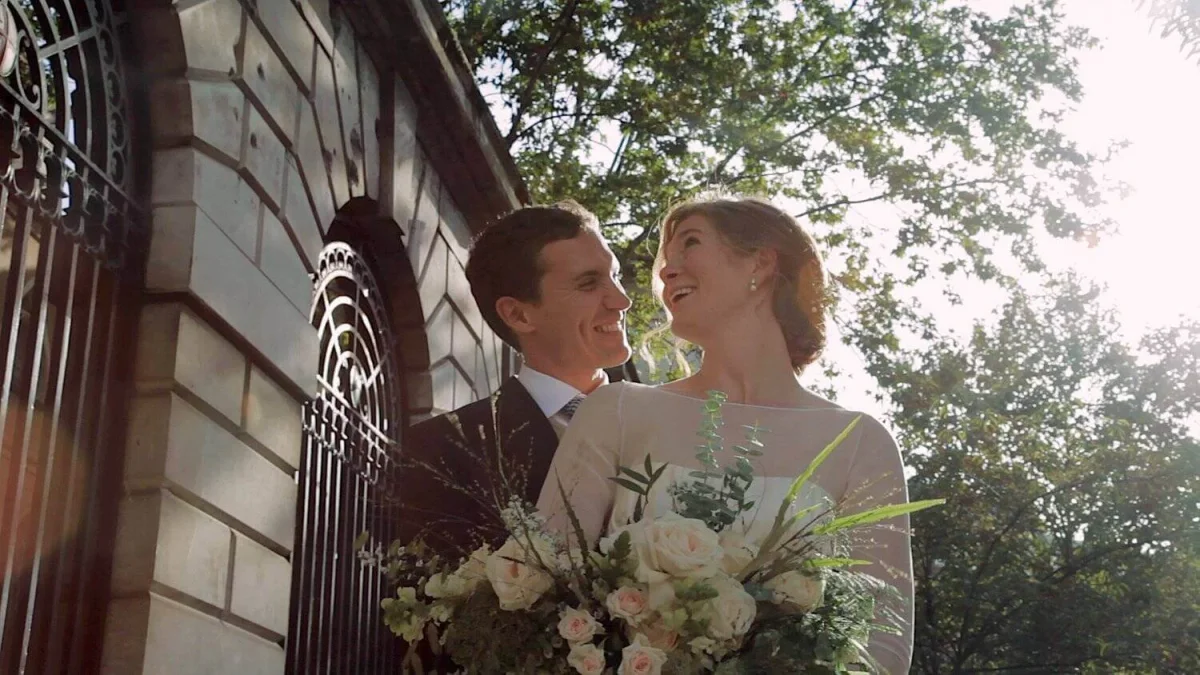 Smiling couple beside an arched iron gate, the bride holding a bouquet of roses