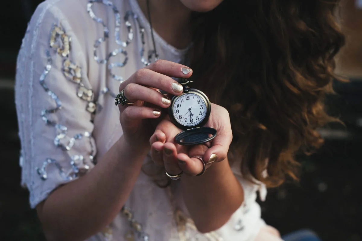 Woman in a sequinned blouse holding an open pocket watch