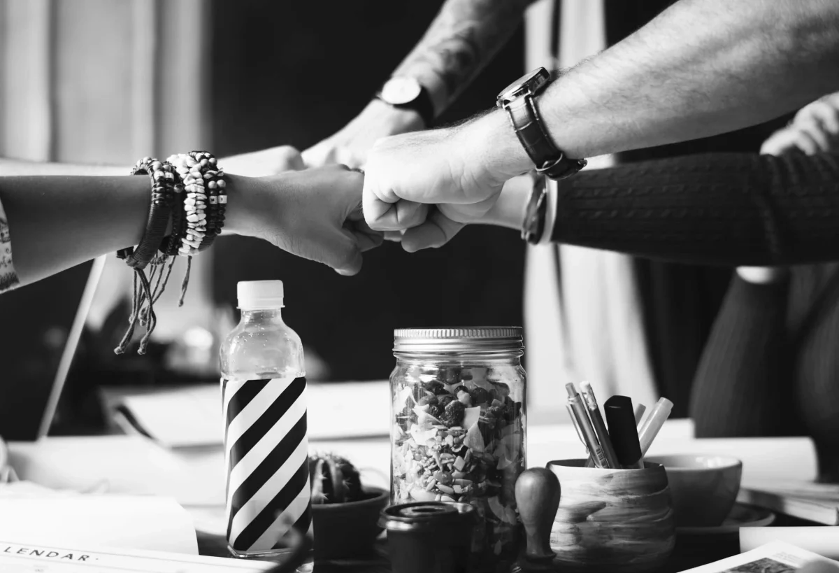 Four people bumping fists over a table of snacks, pens and papers