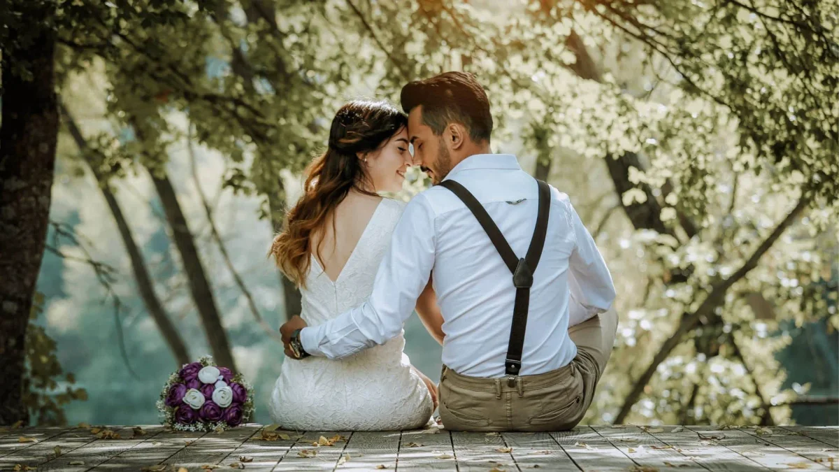 Bride and groom sitting by the river in a romantic setting.