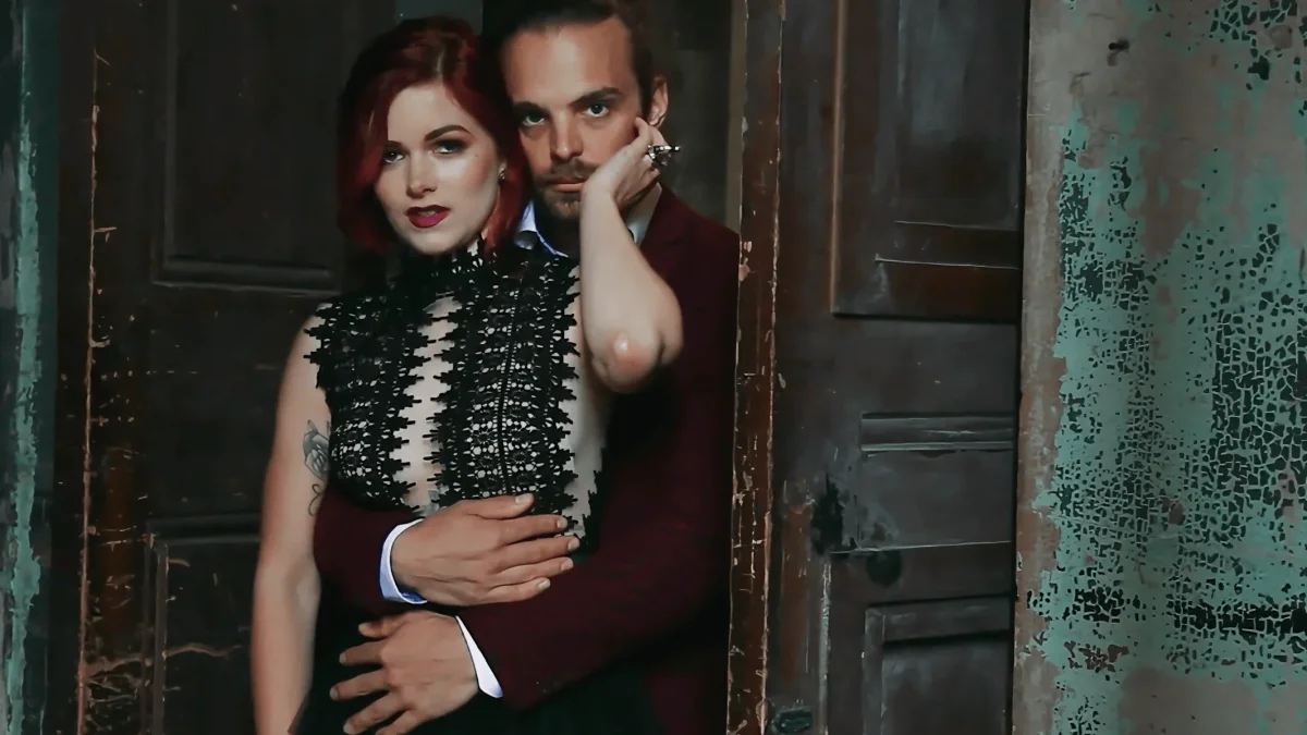 Bride in a black lace dress and groom in a burgundy suit embracing in a doorway at the Asylum Chapel, London