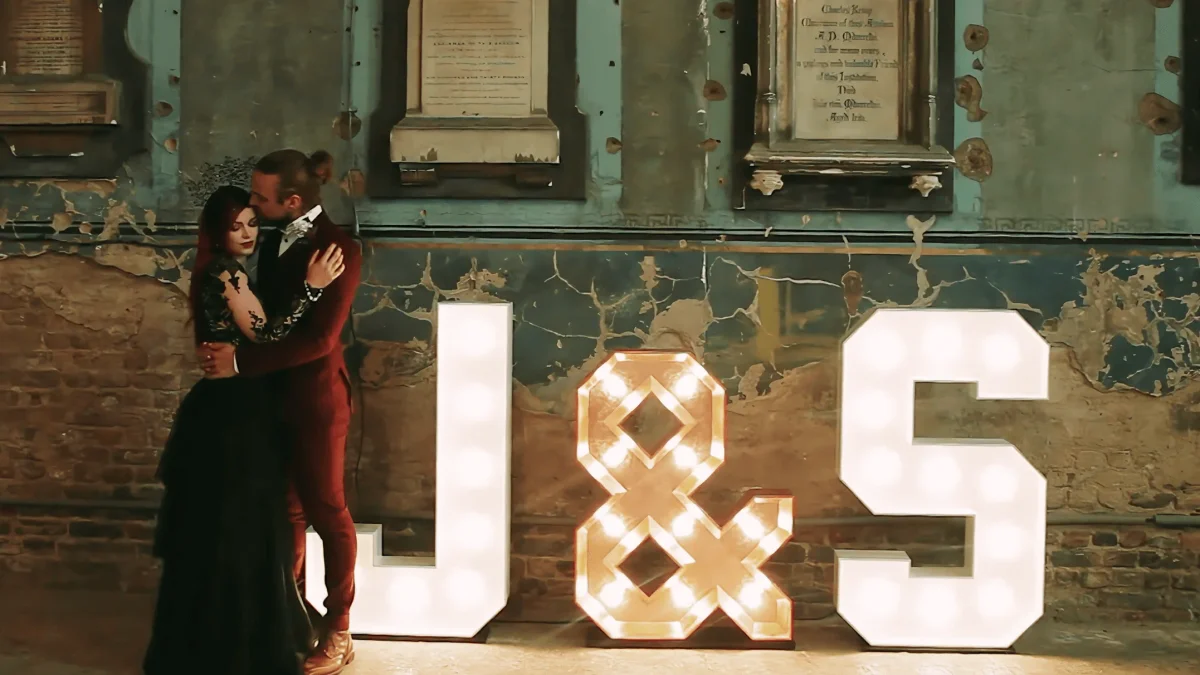 Bride and groom kissing beside illuminated J and S letters at the Asylum Chapel in London