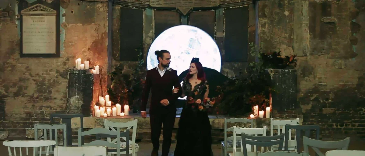 The bride and groom walk down the aisle at their "Nightmare Before Christmas" themed wedding at the Asylum Chapel, surrounded by gothic decor and candlelight.